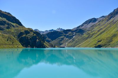 Scenic view of turquoise lake by mountains against clear blue sky