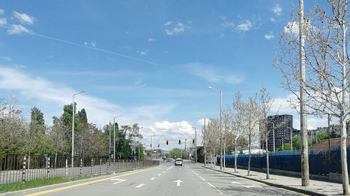 Road by trees against sky in city
