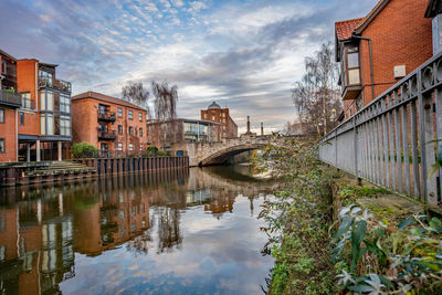 Bridge over canal by buildings against sky