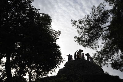 Low angle view of silhouette people standing by trees against sky