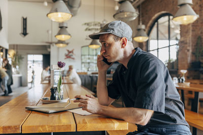 Male owner talking on smart phone while sitting in coffee shop