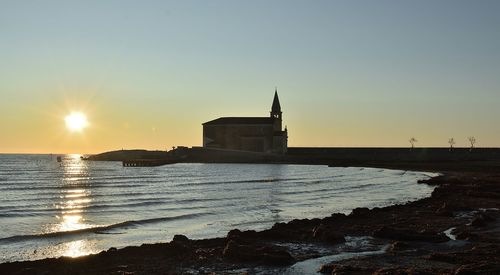 Building by sea against clear sky during sunset