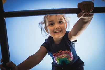 Portrait of smiling girl holding jungle gym against clear blue sky