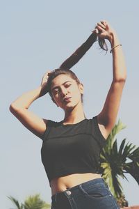 Low angle portrait of young woman standing against clear sky