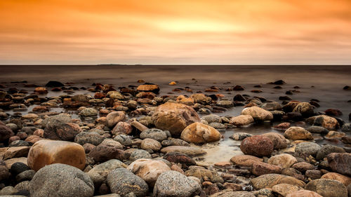 Rocks at beach against sky during sunset