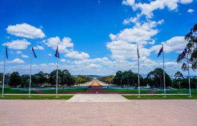 Australian flags at park with walkway leading towards parliament house against sky