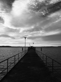 Pier over sea against cloudy sky at sunset