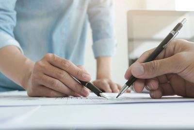 Midsection of man holding paper with pen on table