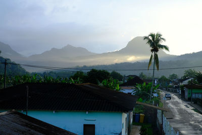 Houses and tree against buildings and mountains against sky