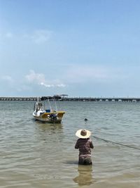 Rear view of man sitting on boat moored in sea against sky