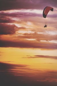 Low angle view of person paragliding against cloudy sky during sunset