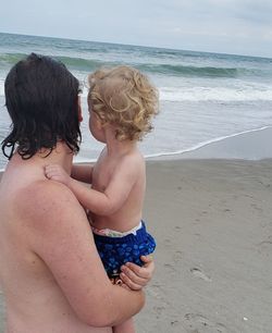 Shirtless father carrying son at beach