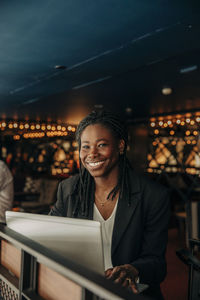 Portrait of happy young female professional sitting with laptop in hotel