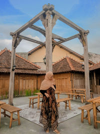 Rear view of woman standing by building against sky