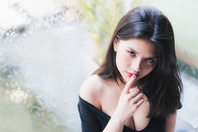 Portrait of young woman with finger on lips sitting by window