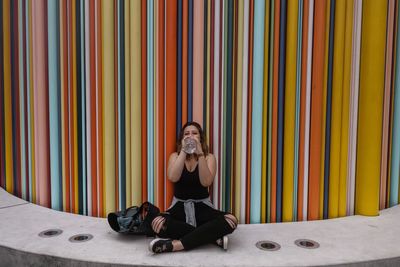 Full length portrait of woman sitting against wall