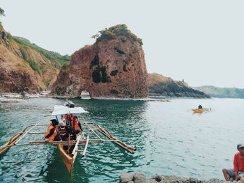 People on rock by sea against clear sky