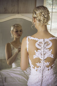 Rear view of bride getting dressed reflecting on mirror