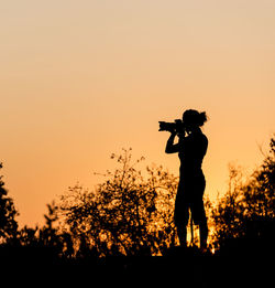 Silhouette man photographing against sky during sunset