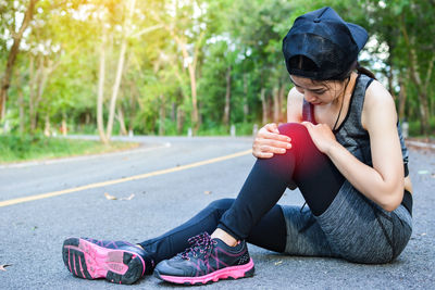 Woman wearing sports clothing with knee pain sitting on road