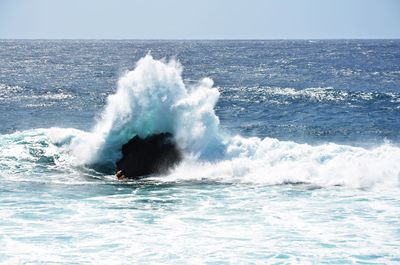Waves splashing on sea against clear sky