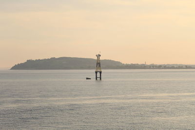 Lighthouse by sea against sky during sunset