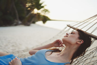 Young woman looking away while sitting on hammock at beach