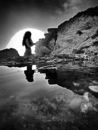 Side view of woman standing on rock against sky