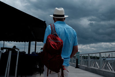 Rear view of man on pier against cloudy sky