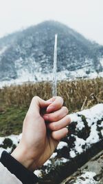 Cropped image of hand holding icicle against mountain