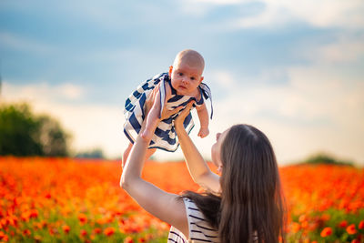 Mother picking up cute daughter amidst plants against sky