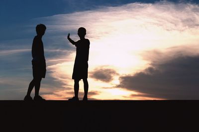 Low angle view of silhouette friends standing against sky during sunset