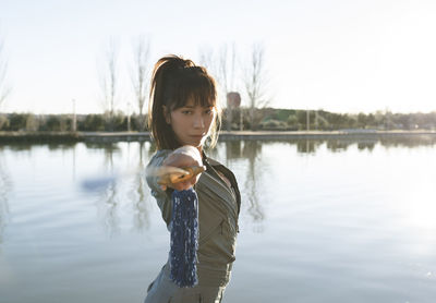 Confident female martial artist holding sword while standing against lake on sunny day