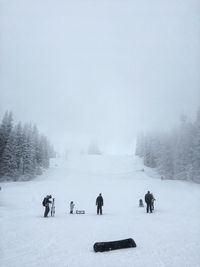 People on snow covered field against trees