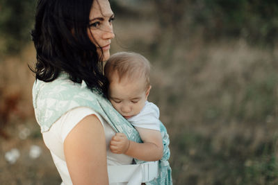 Side view of mother carrying sleeping son while standing on land