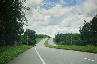 Empty road amidst trees against sky