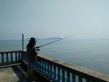 Man fishing by sea against clear sky