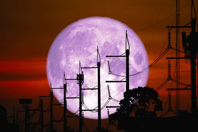 Low angle view of telephone pole against buildings during sunset