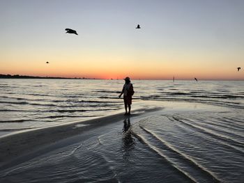 Woman standing on beach against sky during sunset