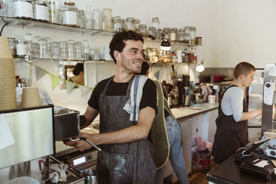 Smiling owner looking away while preparing coffee at cafe