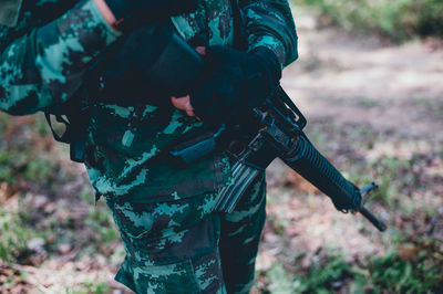 Midsection of person holding gun while standing on land