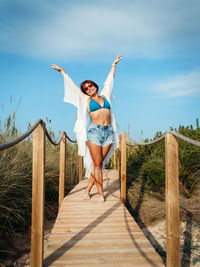 Young woman in white cover up and jeans shorts on a walkway over the dunes