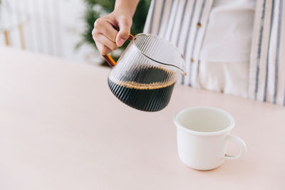 Close up professional barista hand pouring freshly brewed drip coffee in a white mug.