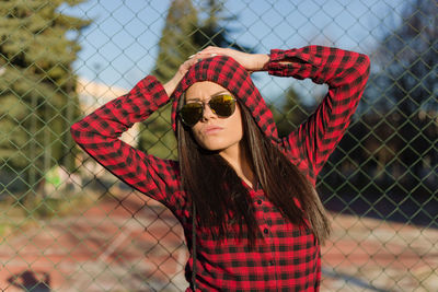 Portrait of young woman wearing sunglasses against fence