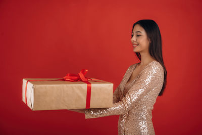Young woman holding gift box against yellow background