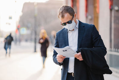 Man wearing mask reading newspaper in city