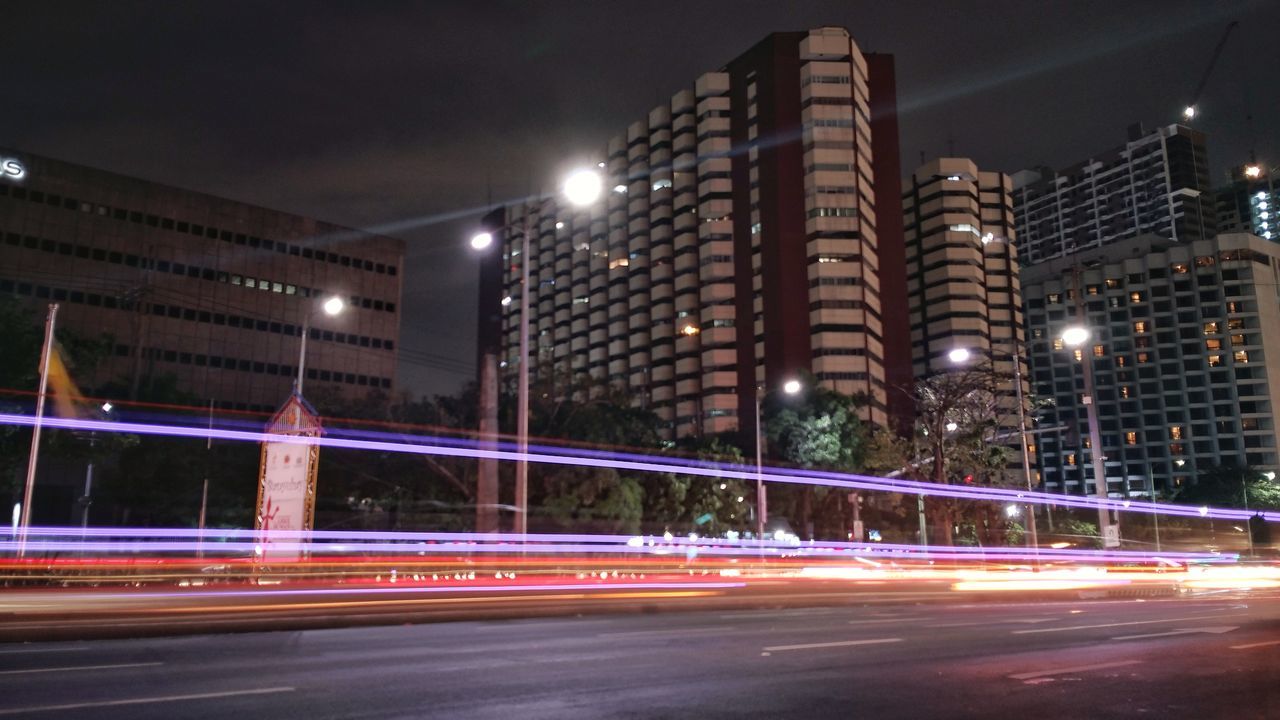 LIGHT TRAILS ON ROAD IN CITY AGAINST SKY AT NIGHT