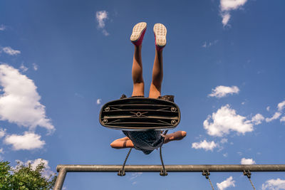 Low angle view of young girl swinging against blue sky at playground