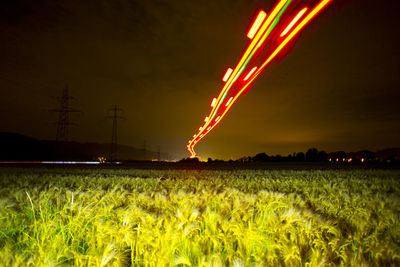 Low angle view of red light trails over field against sky at night