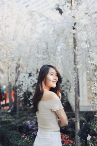 Side view of smiling young woman standing against plants in park